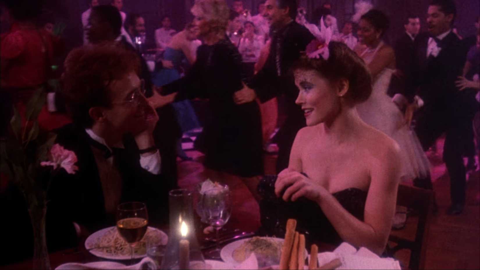 Victor (Reed Birney) sits opposite his crush Nancy (Sheree J. Wilson) at a dining table within an old-timey, pink-lit big-band nightclub, with patrons doing a conga line in the background.