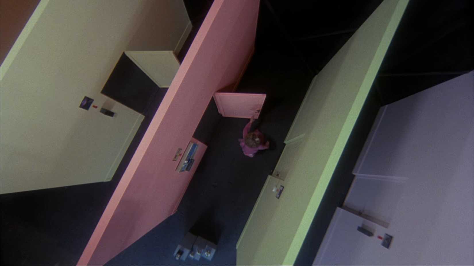 In a bizarre overhead shot from the movie Crimewave, a series of different pastel-colored sample security walls are lined up, as a woman is in the midst of running through each wall's door, shutting them behind her as she goes.