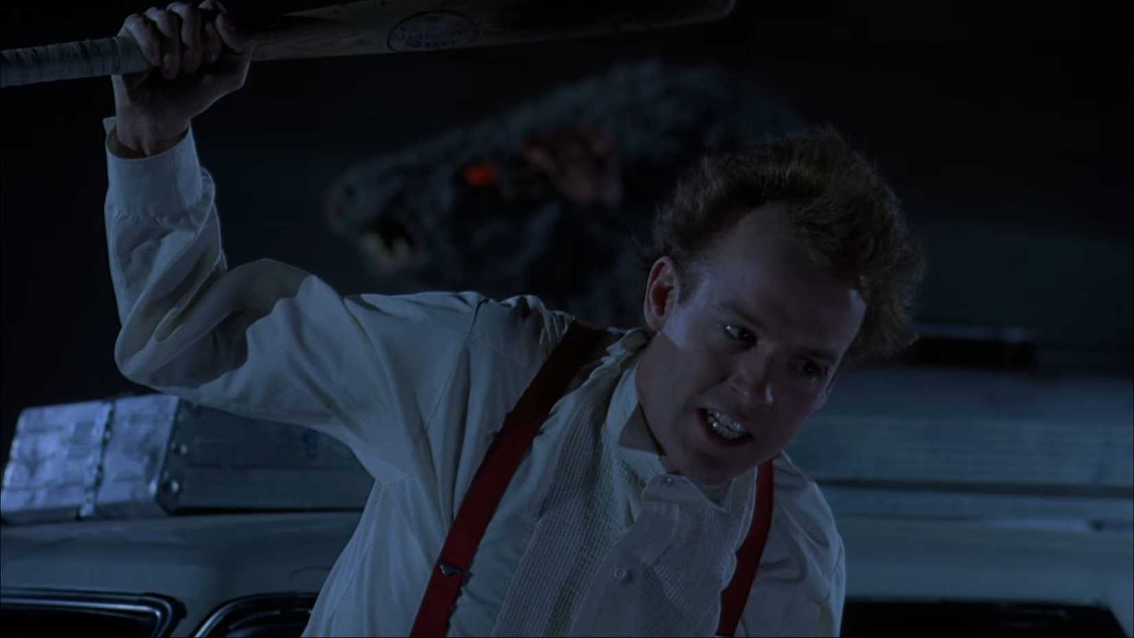 Victor (Reed Birney) brandishes a bat from a moving car window during a night-set car chase from the Sam Raimi film Crimewave.