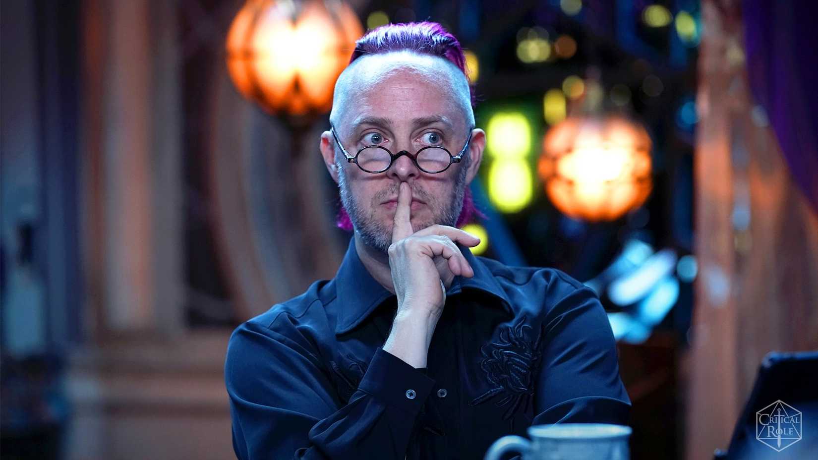 Taliesin Jaffe from Critical Role. He is sat at the table with a finger to his lips.
