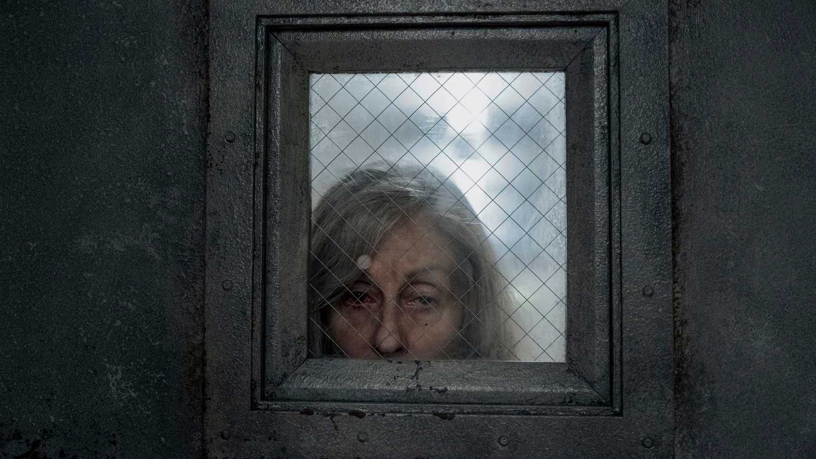 Judith Light, a woman with gray hair, peers through the window of a silver door in The Terror: Devil in Silver