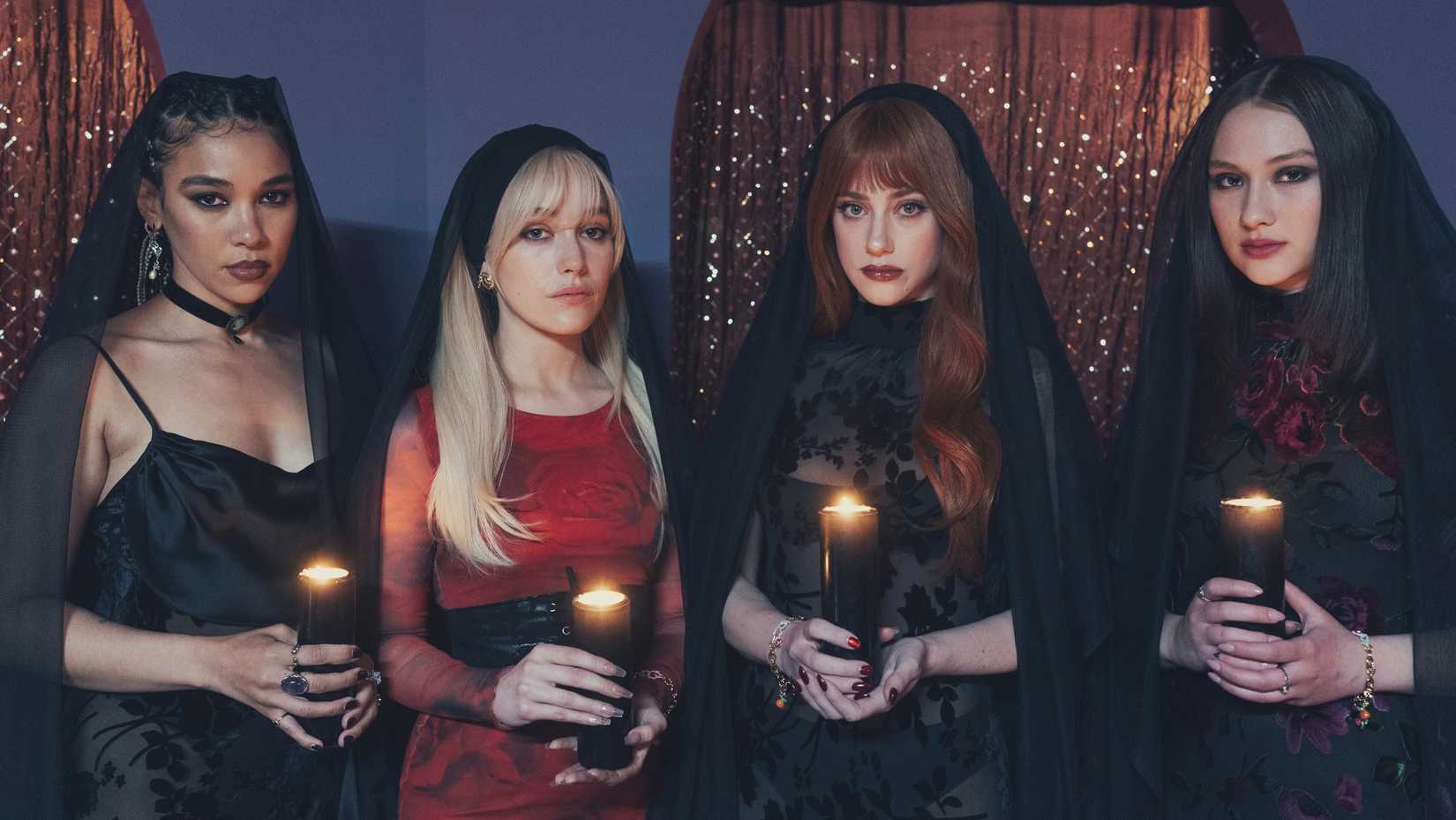 Four fashionably cloaked young women (Alexandra Shipp, Victoria Pedretti, Lili Reinhart, Lola Tung) hold candles facing the camera in a scene from the horror-comedy Forbidden Fruits.