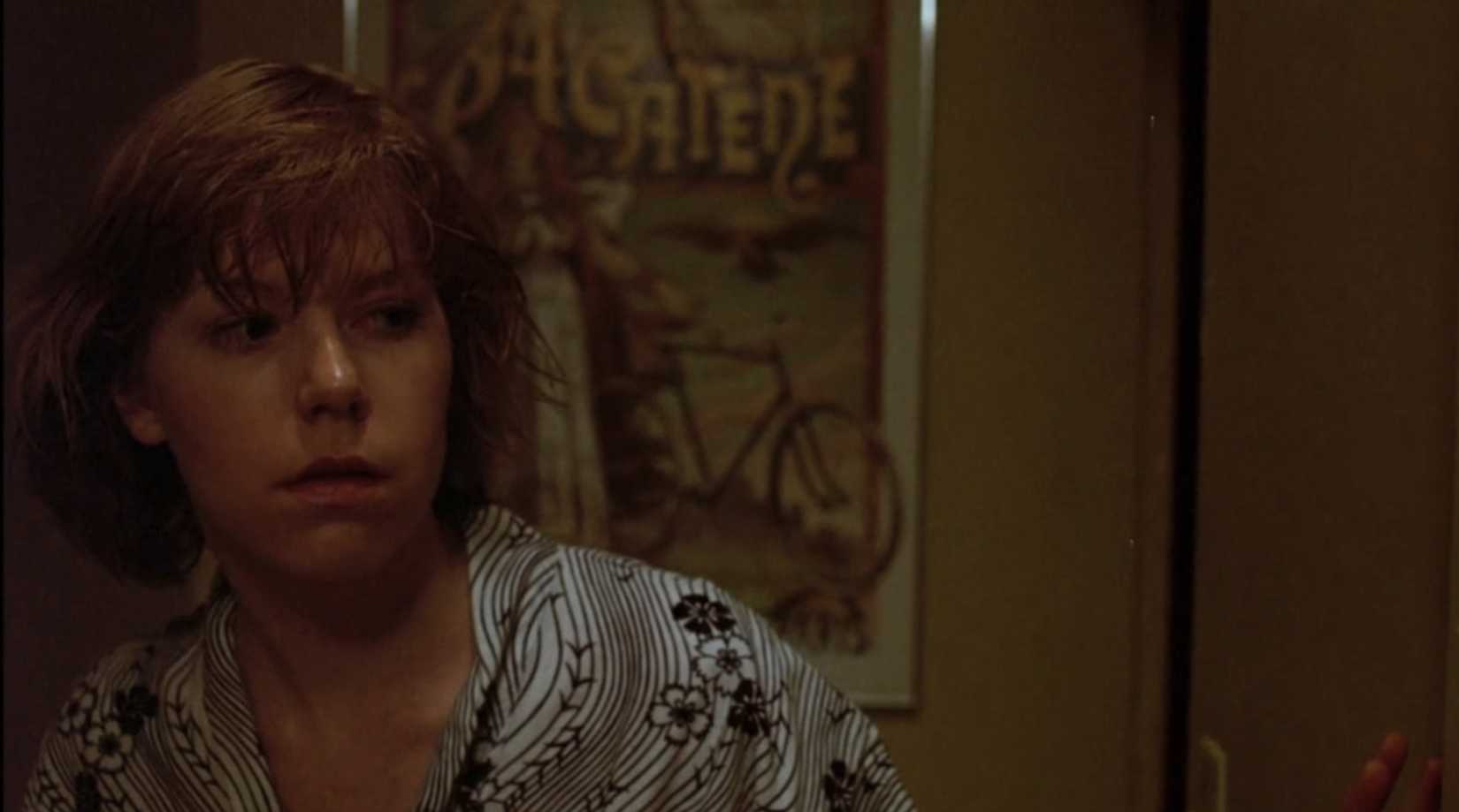 A woman with reddish brown hair nervously peering around the corner in her apartment