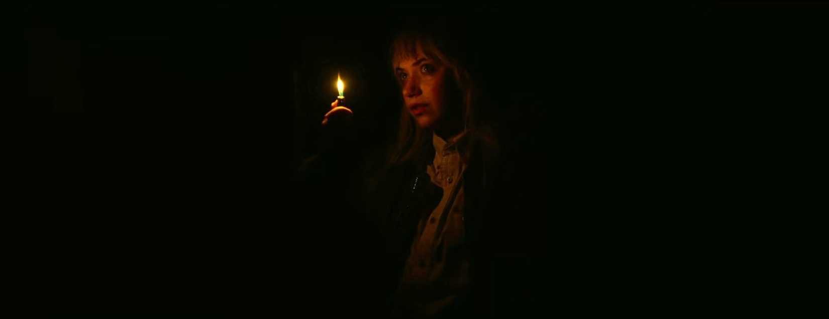 In a tense scene from Green Room (2016), Amber (Imogen Poots) illuminates a pitch-black room with her lighter, making her orange-glowing center-frame image the only visible thing in a sea of blackness.