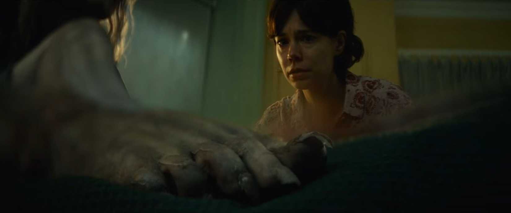 In a split-diopter shot from Lee Cronin's The Mummy, a young girl's grayish, gnarled-looking foot is seen in extreme close-up, while her mother's concerned face is also in sharp focus in the background, with the space between them blurry.