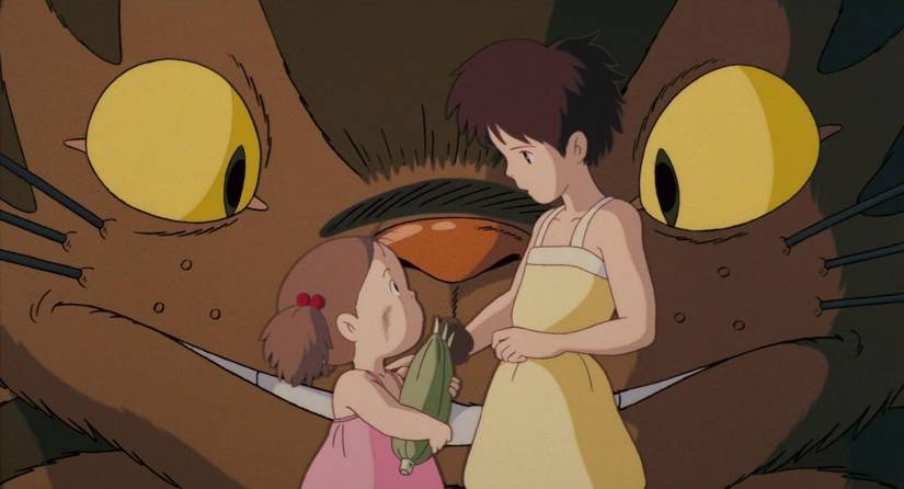 Two young girls speak to each other as a large cat (who is also a bus) watches in My Neighbor Totoro