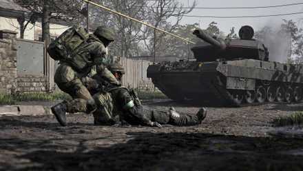 A soldier in Wardogs dragging a fallen ally across the road as a tank advances toward them.