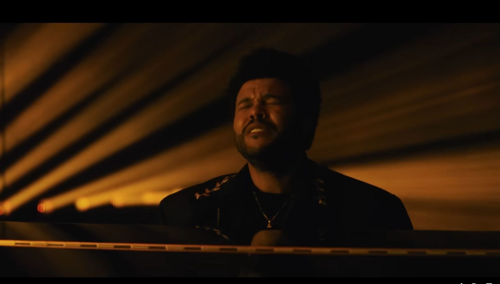 The Weeknd, as he sings a song in front of a piano. 