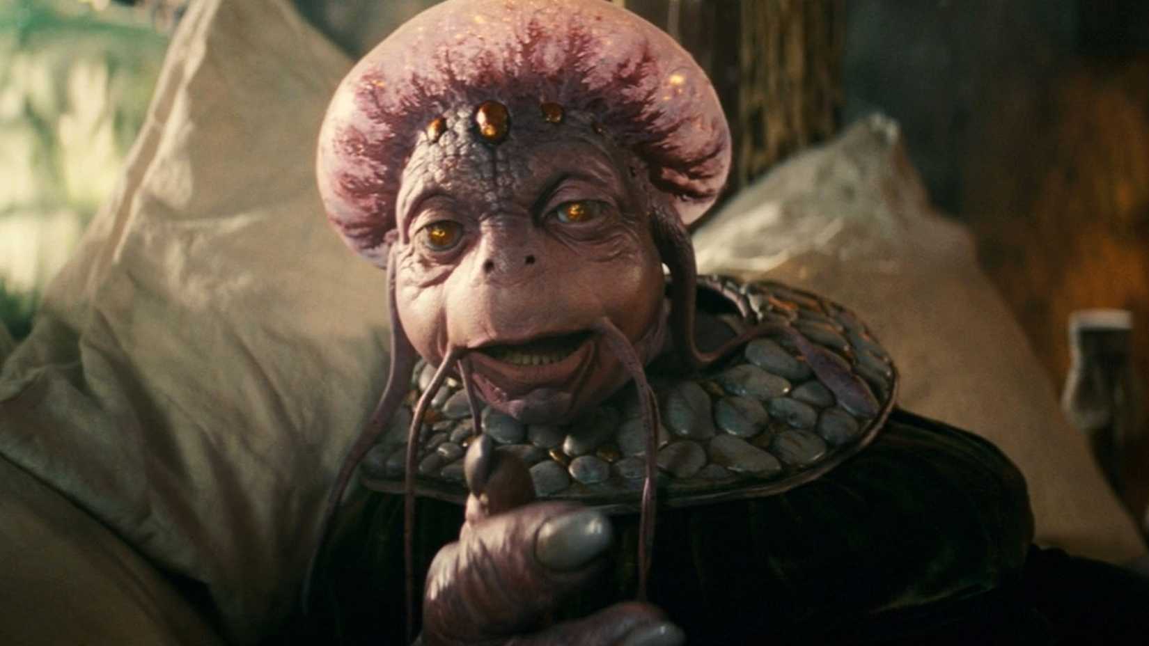 A lizard-like humanoid puppet with glassy eyes and a bulging head reclines in his bed in a scene from the 2011 fantasy comedy Your Highness