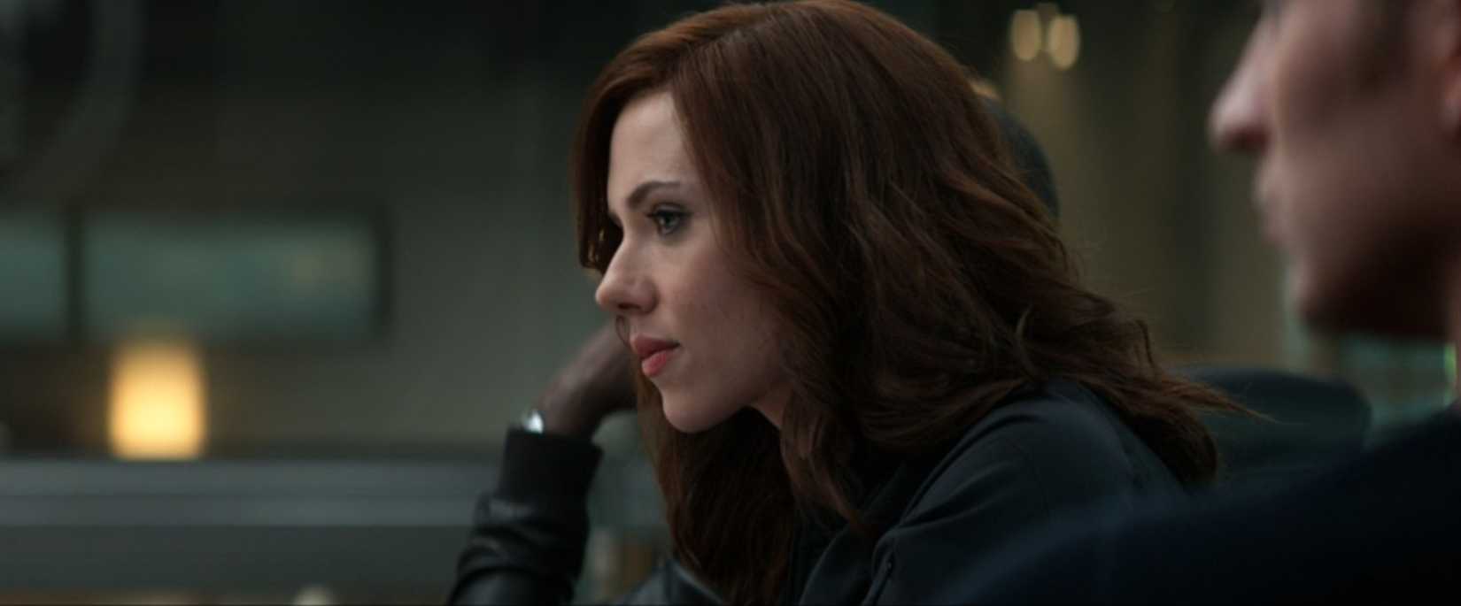 Black Widow (Scarlett Johansson) looks pensive in a medium-close-up profile shot, sitting in a government office in a scene from Captain America: Civil War