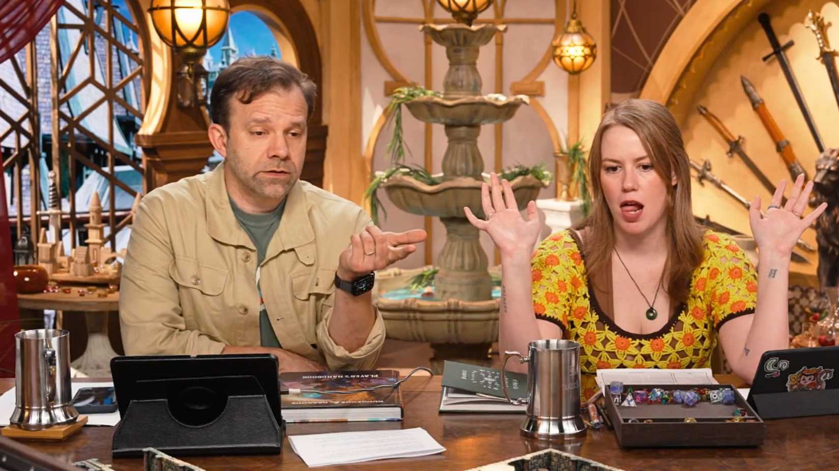 An image showing Critical Role's Liam O'Brien and Marisha Ray sitting side by side at the Critical Role table.