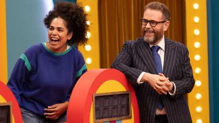 Sam Reich and Kimia Behpoornia stand next to a rainbow-hued podium on the set of Game Changer