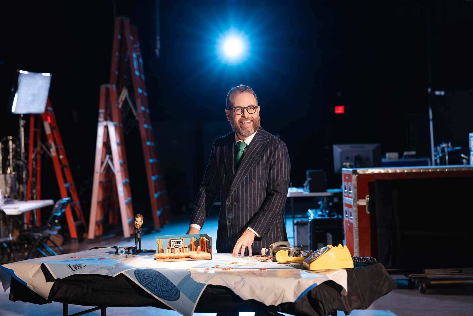 Dropout CEO Sam Reich stands in a dark studio at a table, smiling