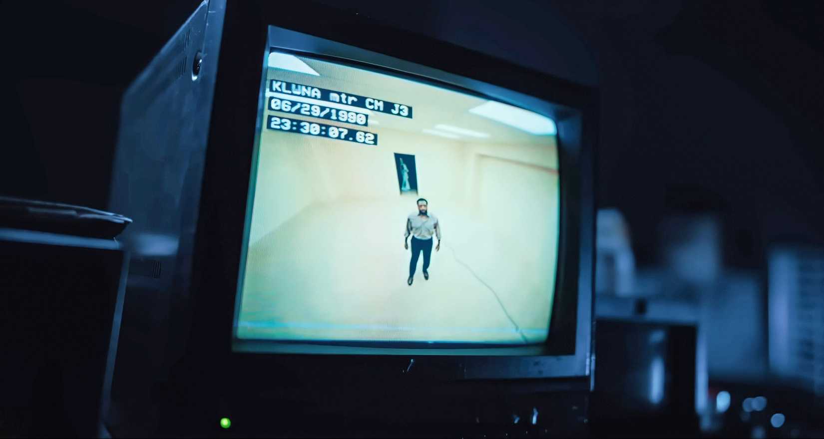 A Black man (Chiwetel Ejiofor) in a button-down shirt and black slacks stands in an empty yellow room, as seen from above on a TV screen displaying security camera footage, in Backrooms