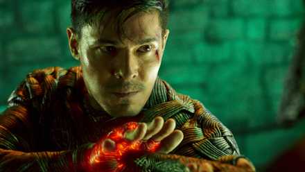 Cole Young (Lewis Tan), a bloodied, sweaty young man wearing glowing woven armor, looks determined in Mortal Kombat 2