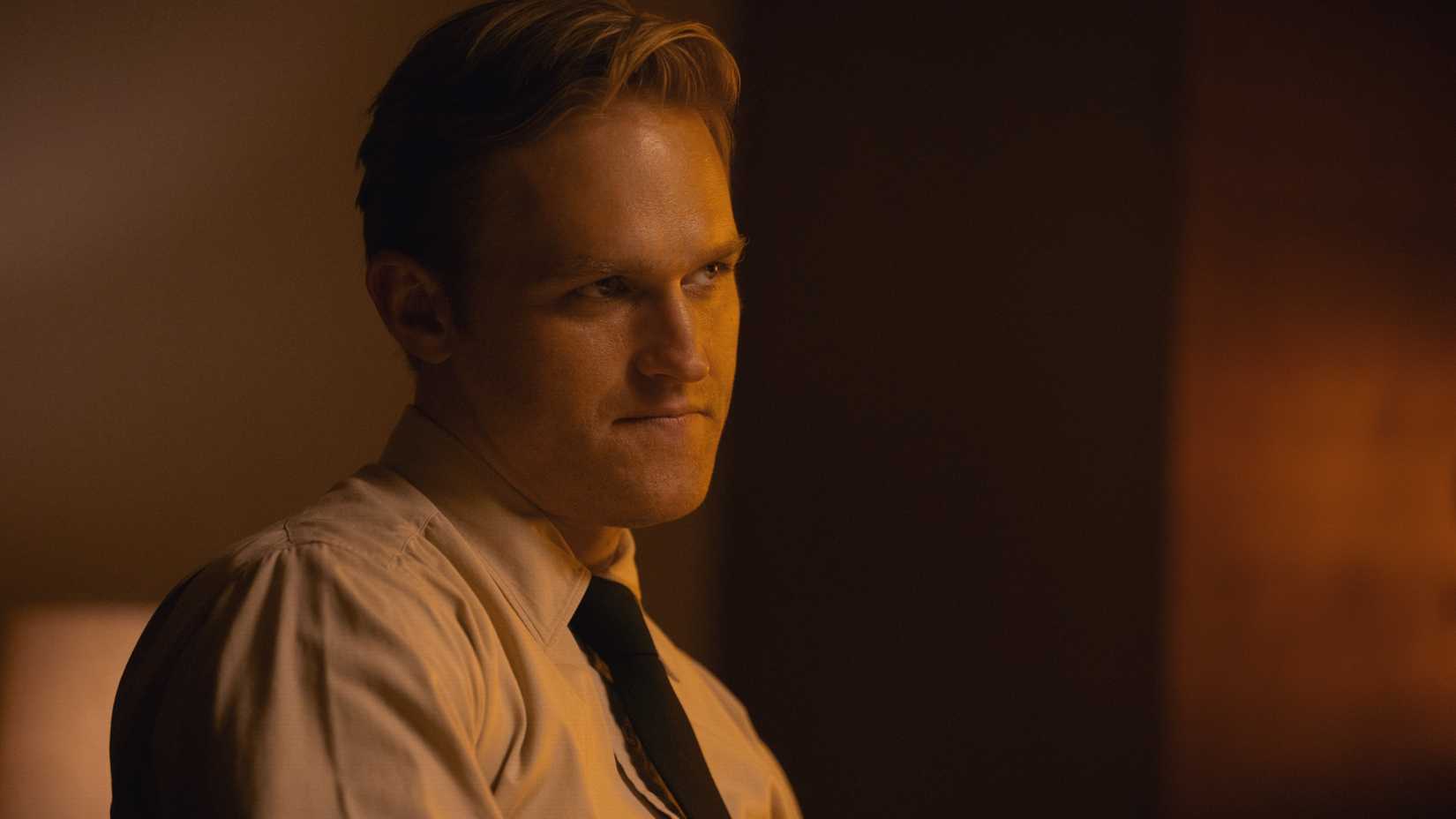 Young Lee Shaw (Wyatt Russell) wearing a white dress shirt and black tie sits in an office and looks dubious in Monarch: Legacy of Monsters season 2.