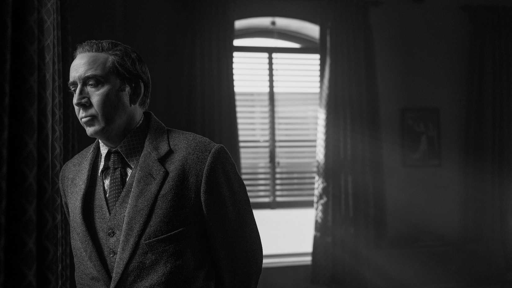 Ben Reilly (Nic Cage) wearing a suit and frowning stands in front of window in Spider-Noir.