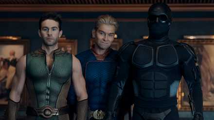 Homelander (Antony Starr) stands behind The Deep (Chace Crawford) and Black Noir (Nathan Mitchell) in Vought Tower as Deep looks very nervous.