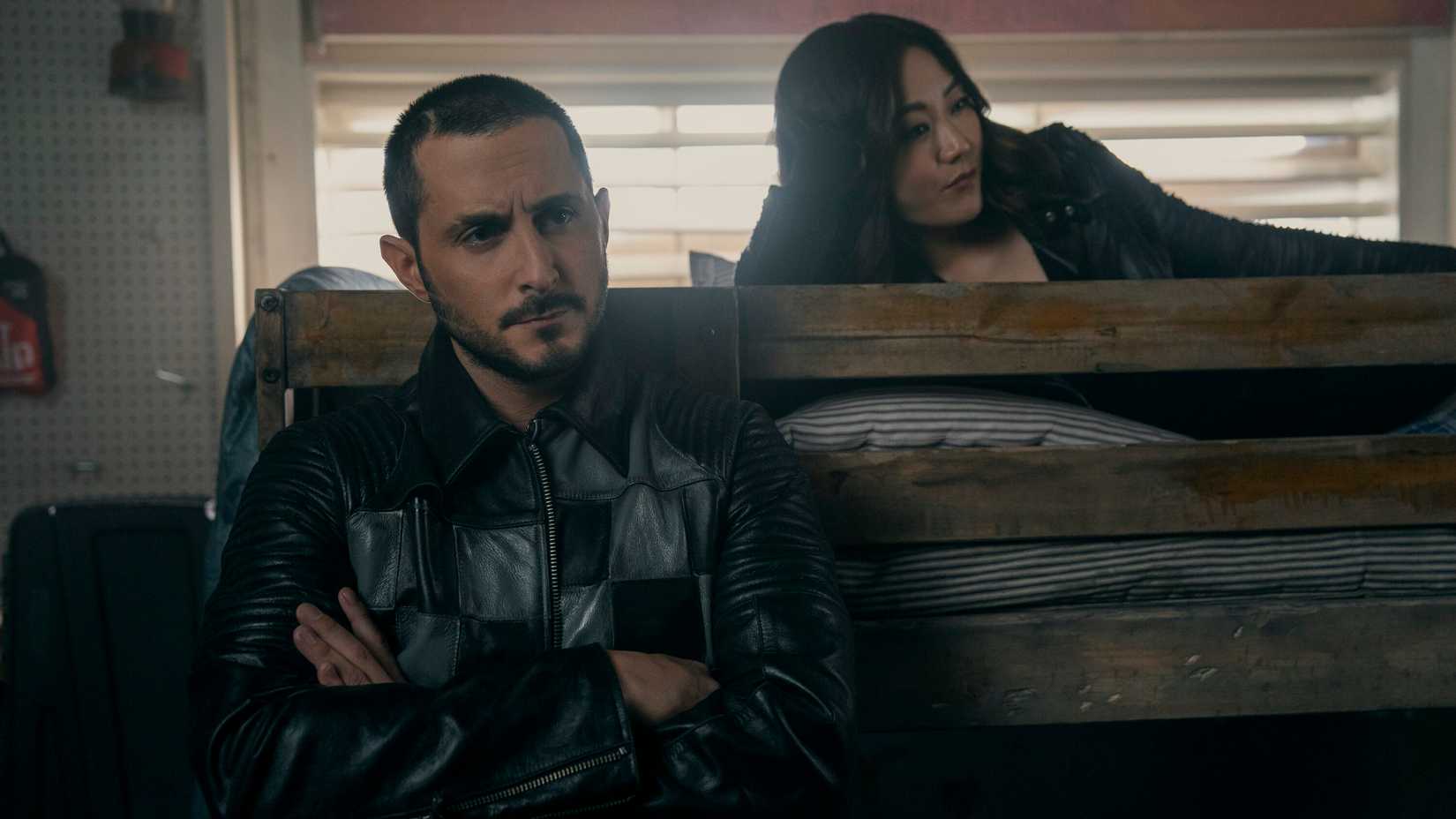 Kimiko (Karen Fukuhara) lies on the top of a bunkbed while Frenchie (Tomer Capone) leans against it with his arms folded.