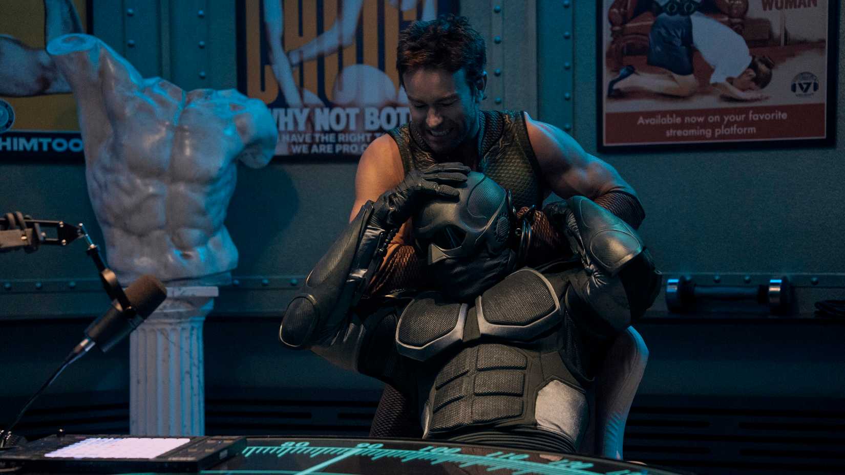 The Deep (Chace Crawford) holds Black Noir (Nathan Mitchell) in a chokehold while he sits at a table and tries to struggle in The Boys.