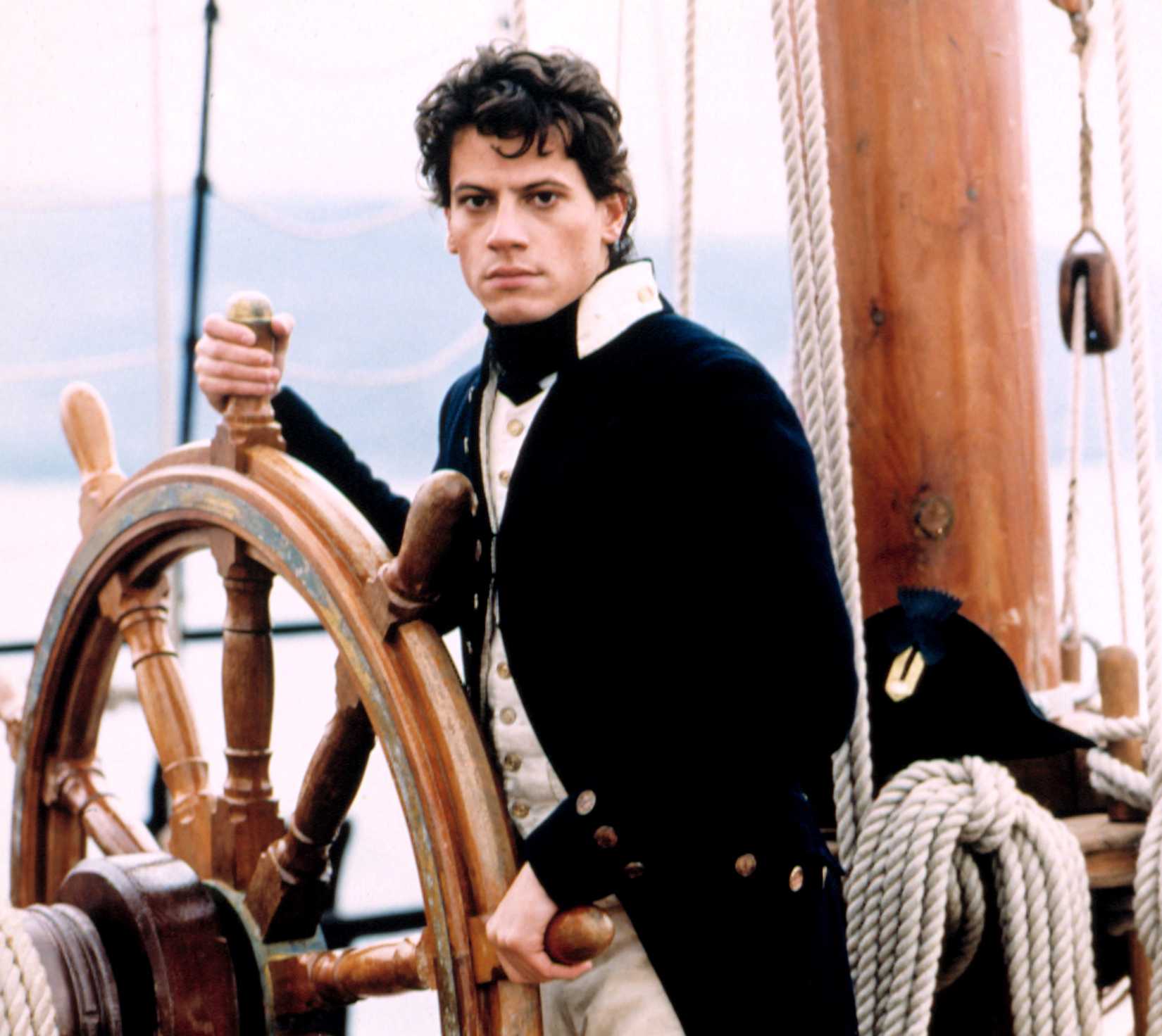 Ioan Gruffudd as Lieutenant Horatio Hornblower, a young, pale man in a British Navy uniform, at the wheel of a ship, in A&E Network's Horatio Hornblower series