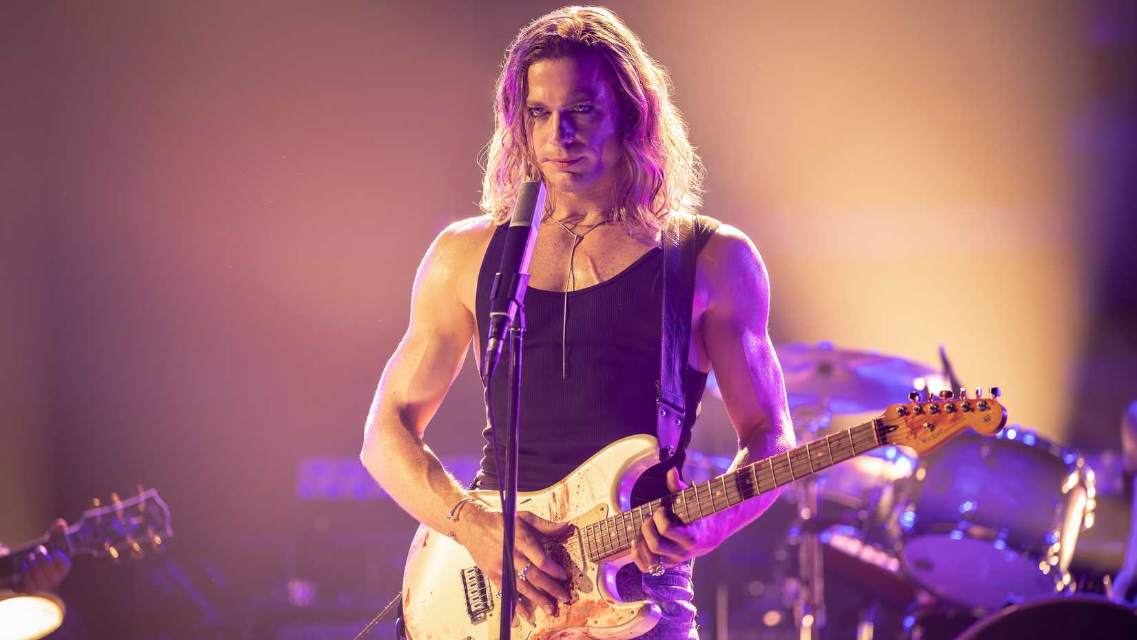 Lestat (Sam Reid) wearing a black tanktop plays electric guitar on stage in The Vampire Lestat.