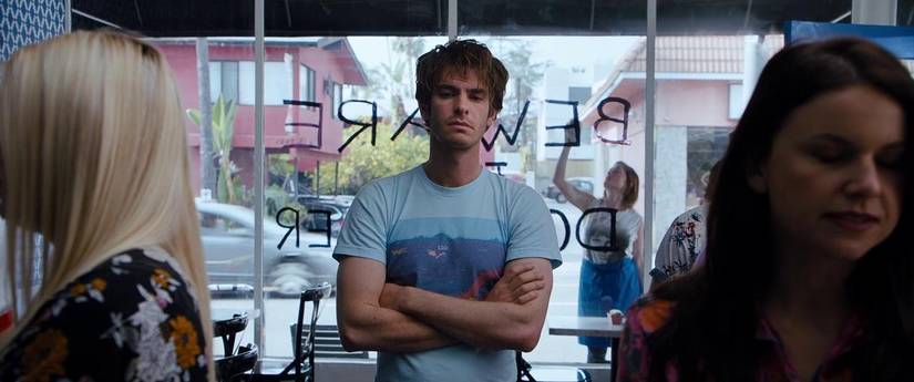 Sam crosses his arms and stares blankly ahead in Under the Silver Lake