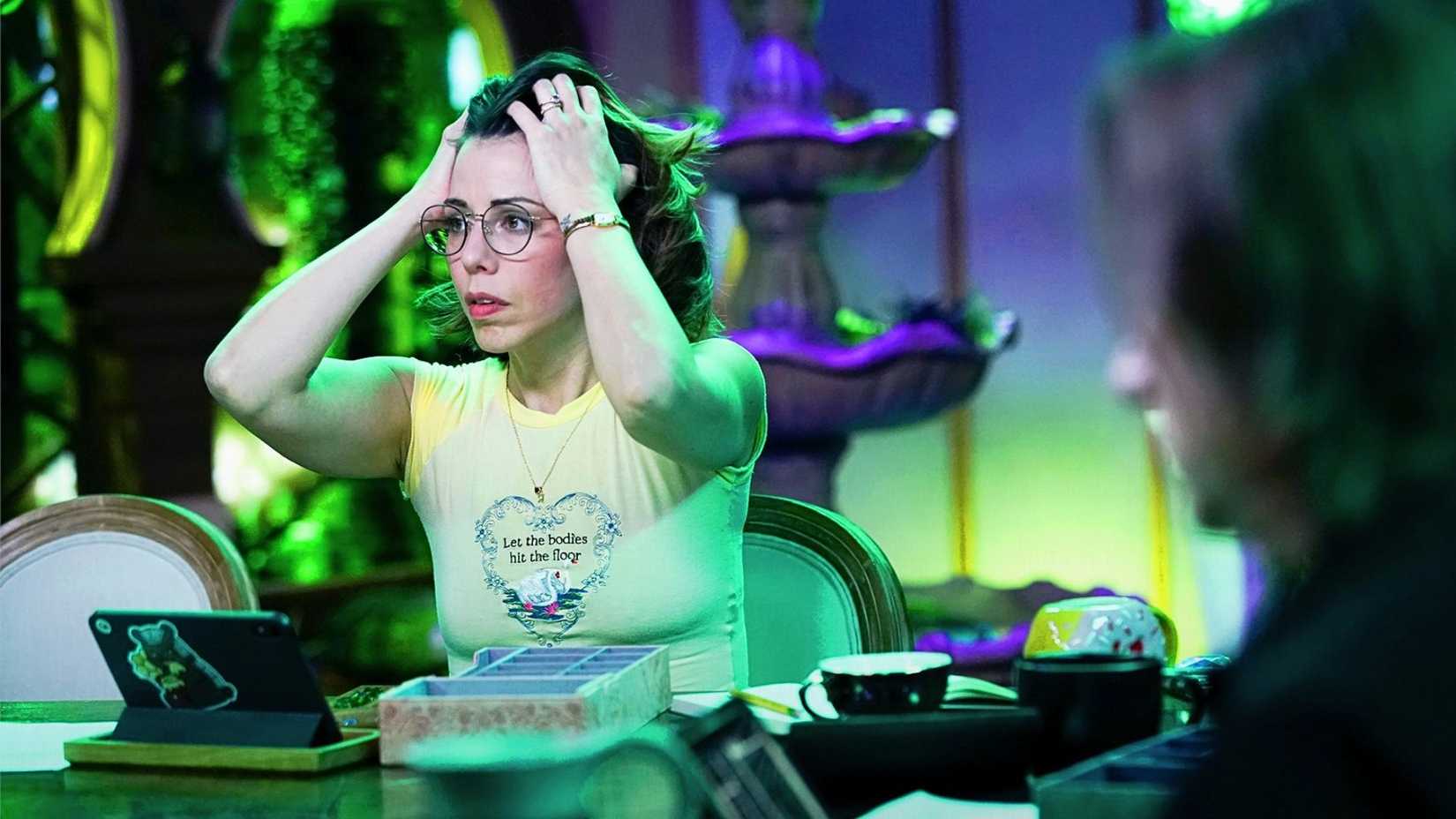 Critical Role's Laura Bailey sits at a table. She looks visibly stressed.