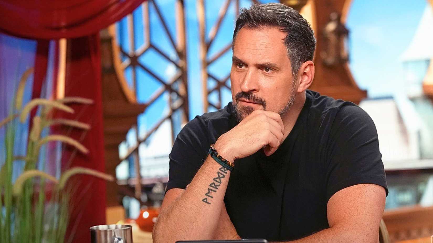 Critical Role's Travis Willingham sits at a table, looking serious.