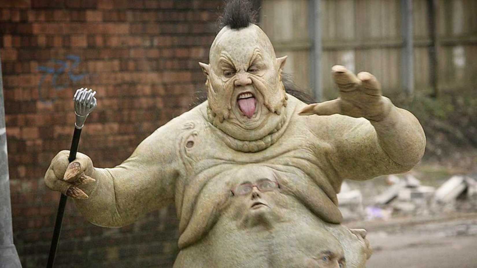An image of Peter Kay as the Abzorbaloff, a green alien with a cane in its hand. It runs forward, tongue brandished out of its mouth.