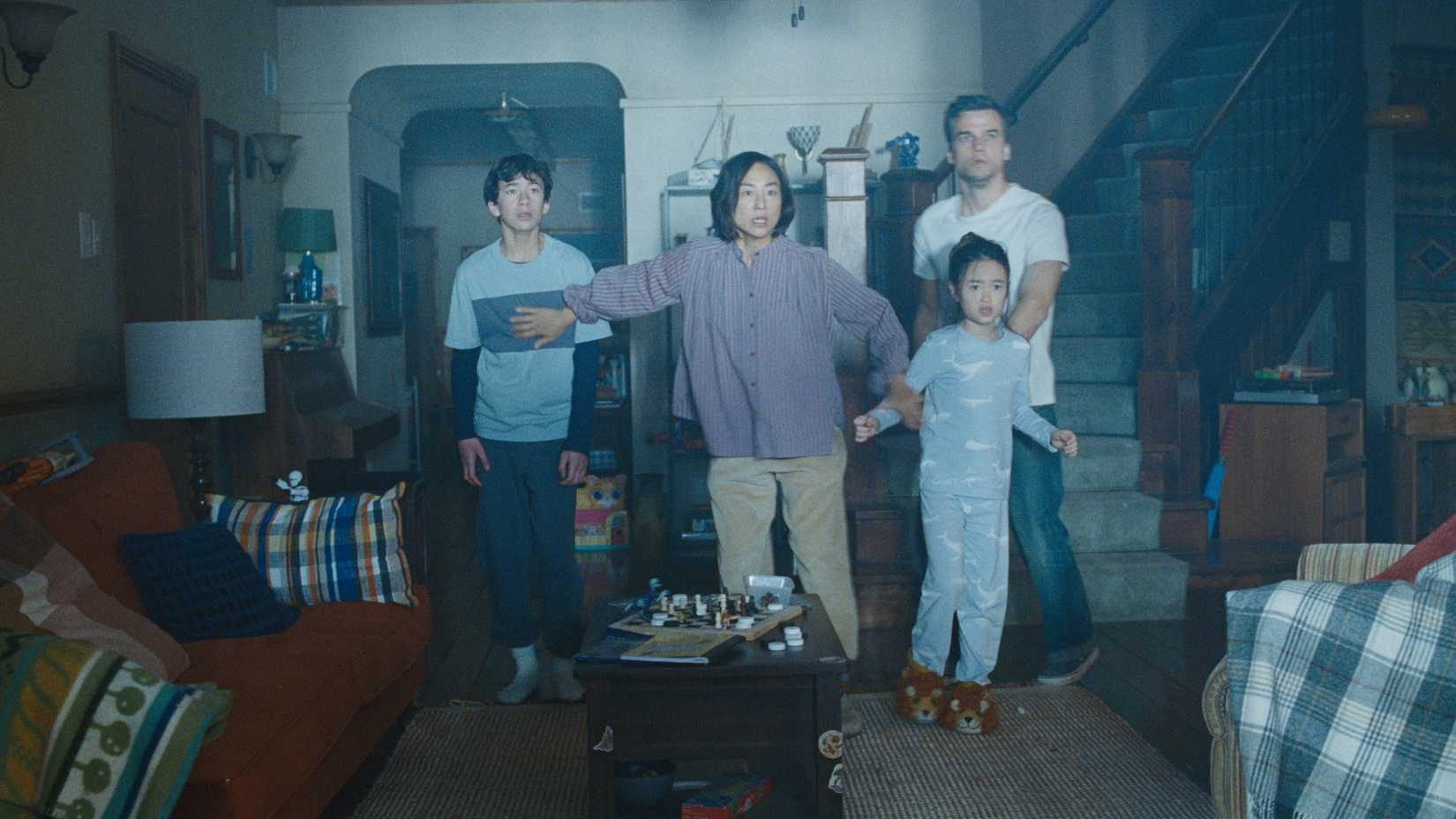 An image from The Last House from Netflix. IT shows a family of four standing together in their house in the dark. A bright light outside shocks them.