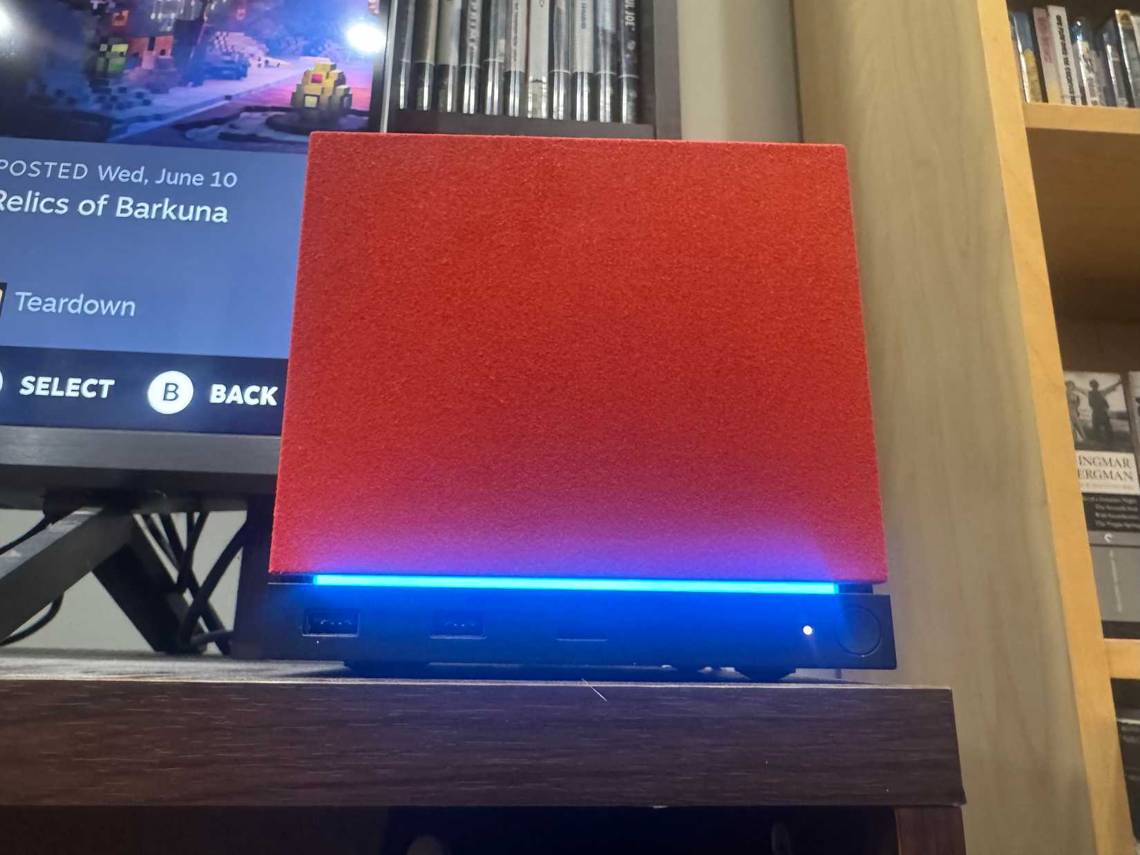 A Steam Machine with a red faceplate sits on an entertainment center.