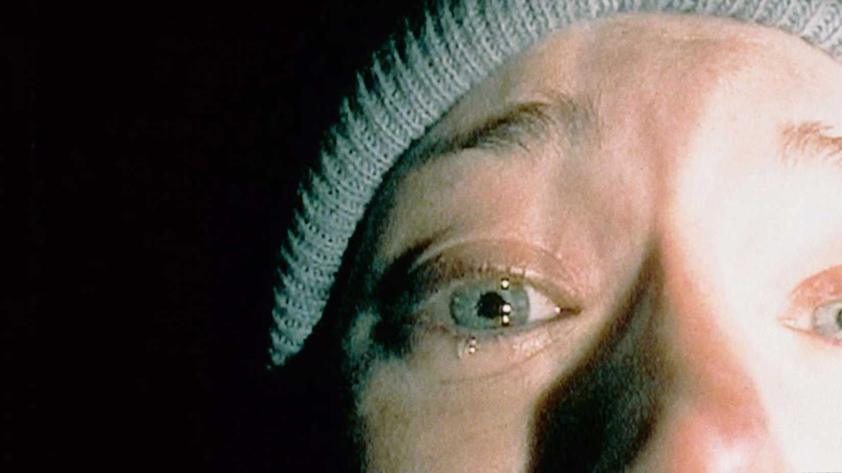 A closeup of half a woman's face against darkness, a single tear coming from her right eye.