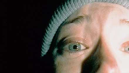 A closeup of half a woman's face against darkness, a single tear coming from her right eye.