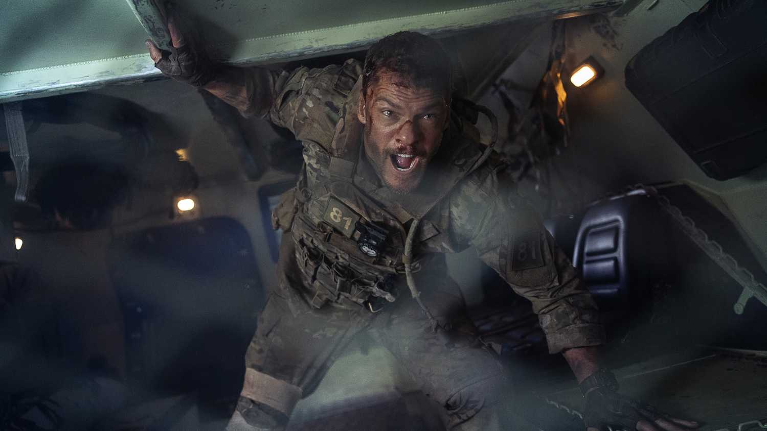 81 (Alan Ritchson) hét lên bên trong một chiếc xe vận tải bọc thép trong một cảnh quay từ phim War Machine của Netflix