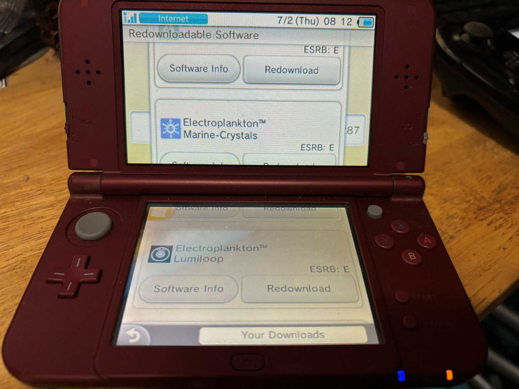 A red Nintendo 3DS console sits open with a screen offering a redownload of Electroplankton Lumiloop