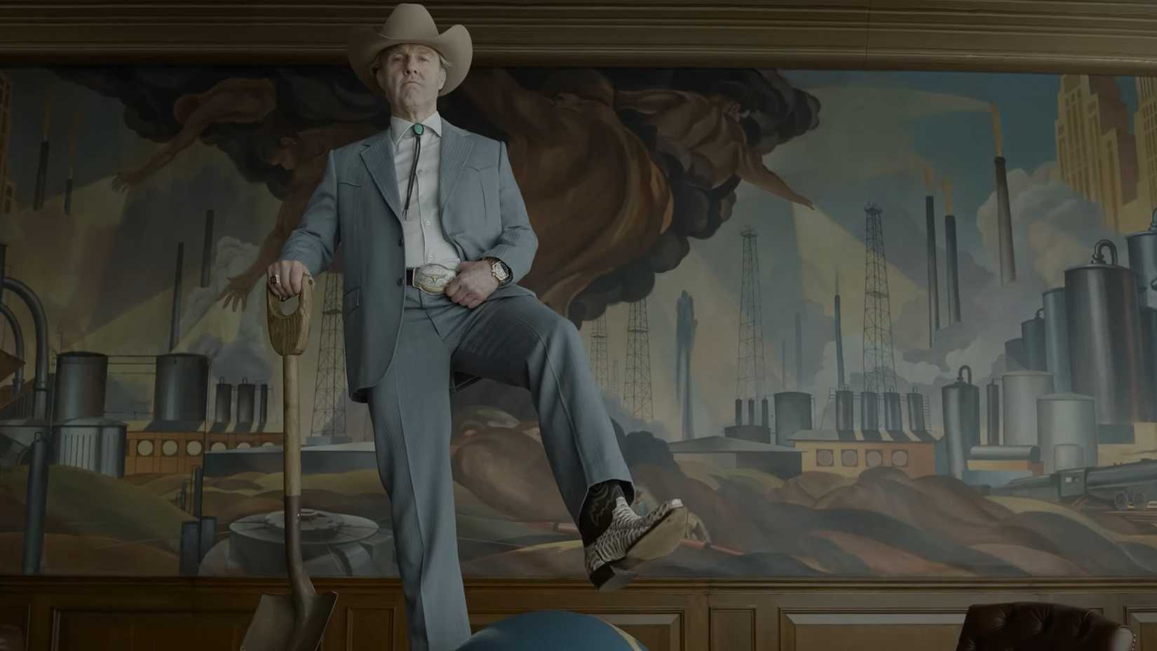 Tom Cruise as Digger stands on a table in a suit wearing a cowboy hat and boots and holding a shovel