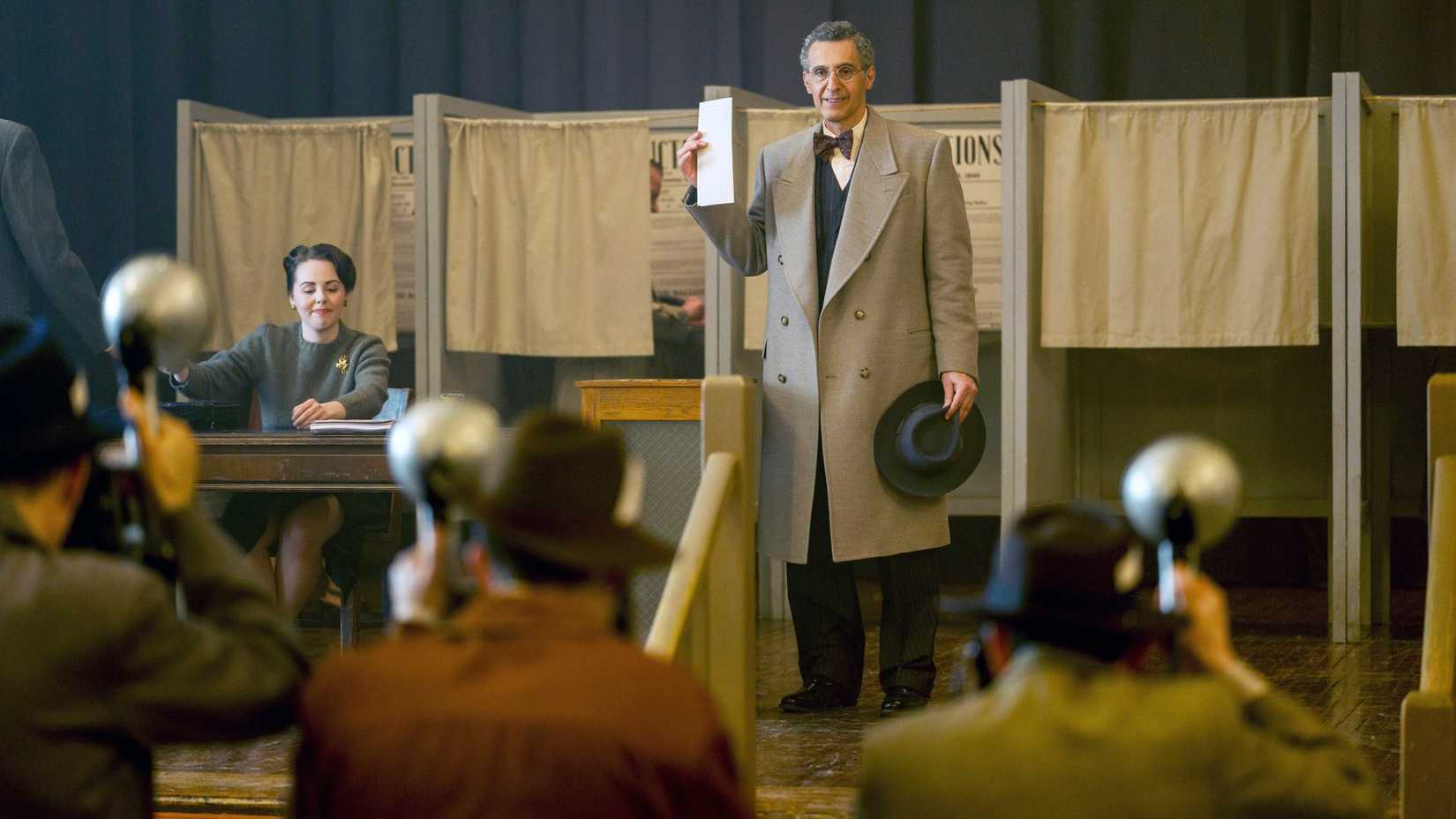 John Turturro holds a ballot outside an election booth while reporters snap photos in the Plot Against America.
