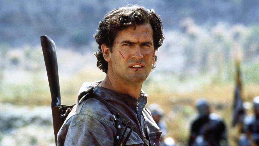 Bruce Campbell's Ash smirks while carrying a gun during the Middle Ages in Army of Darkness
