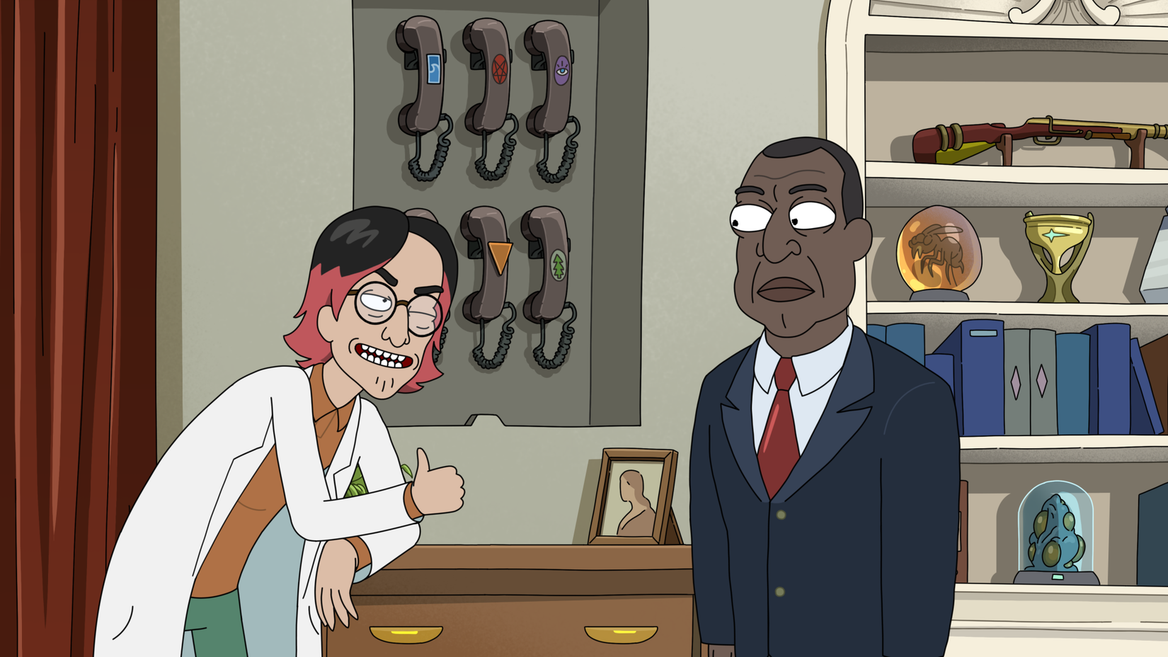 A guy wearing a lab coat winks at President Curtis and gives him the thumbs up while leaning on a desk near a rack of phones with odd logos.