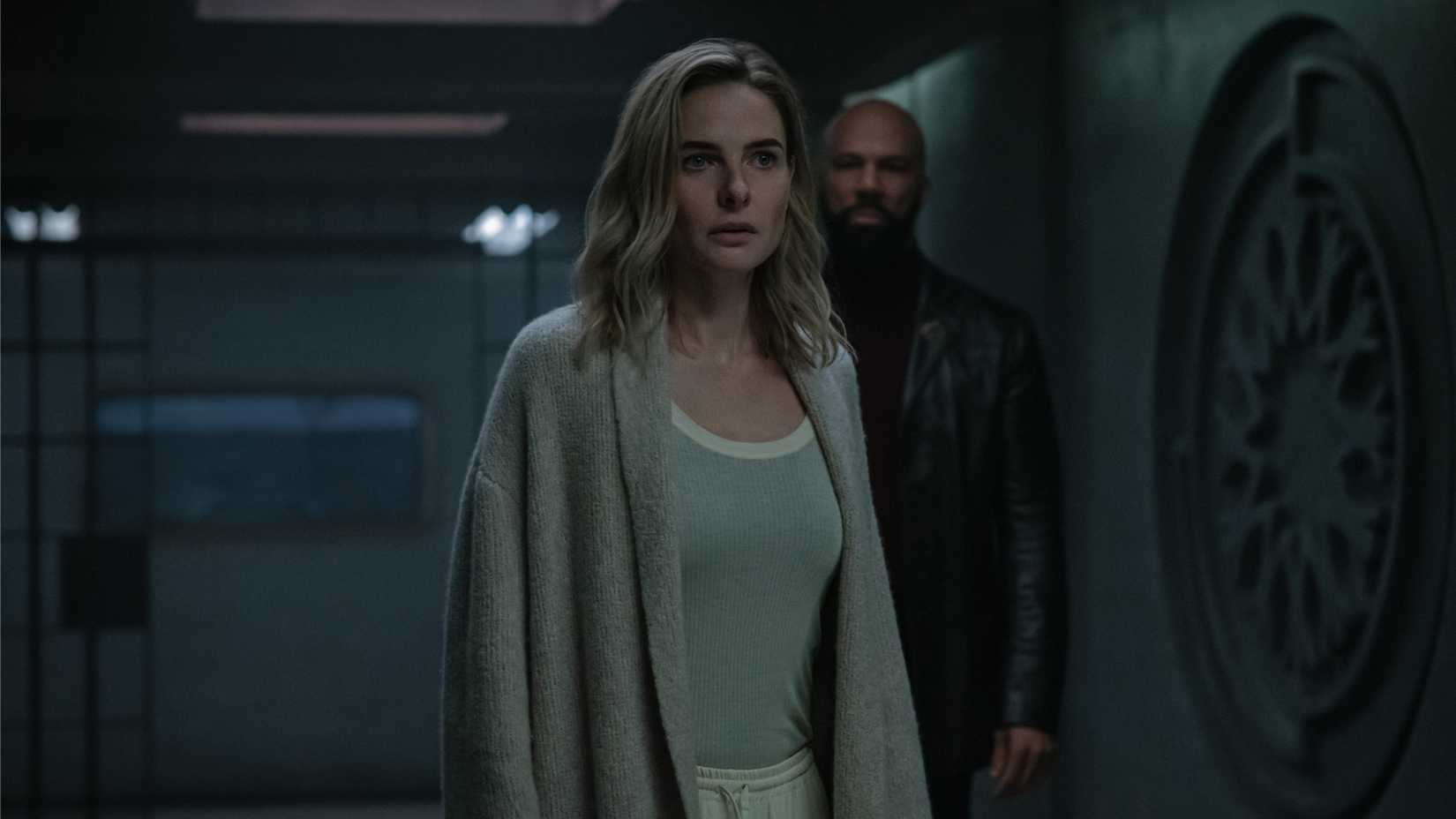 Juliette Nichols (Rebecca Ferguson) wearing a sweater and pajamas stands in front of Robert Sims (Common) near an open prison cell in Silo.