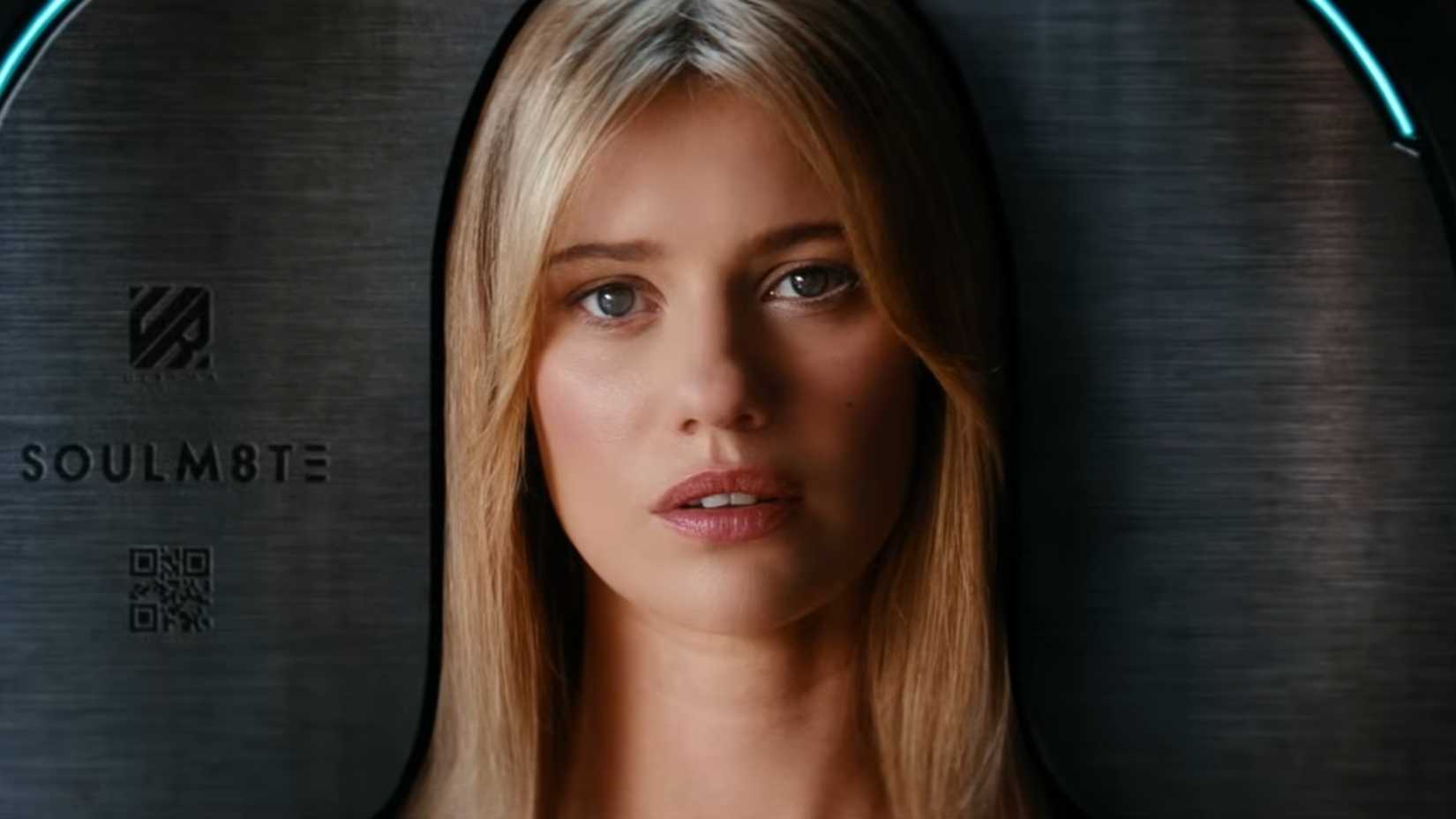 A blonde woman staring at the view from a metal coffin ingraved with the word "SOULM8TE"