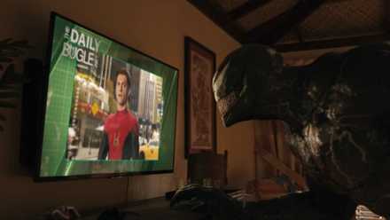 Venom watches Spider-Man on a hotel TV in a still from Venom: Let There Be Carnage