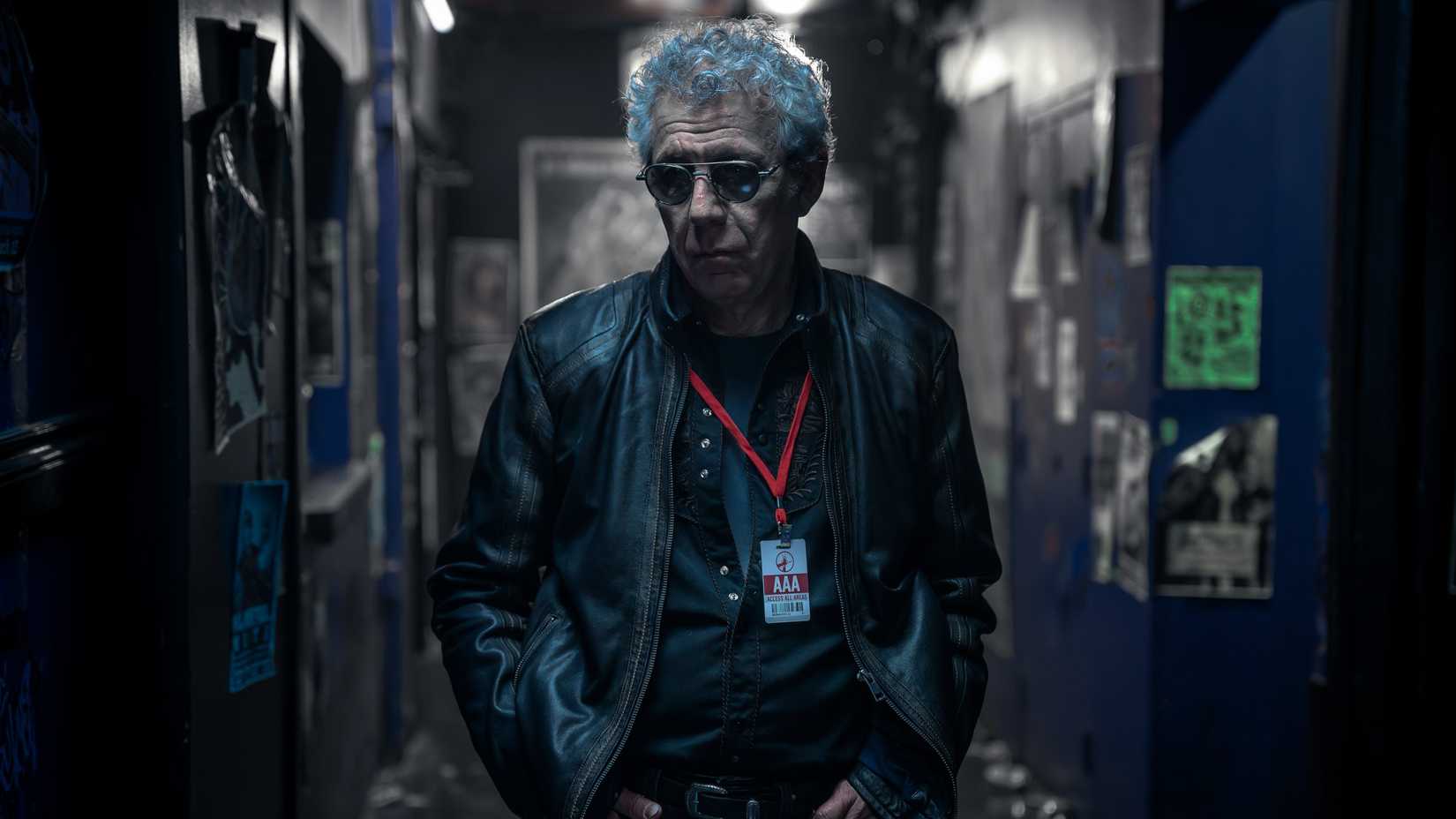 Daniel Molloy (Eric Bogosian) đeo kính râm và áo khoác da khi đi sau hậu trường