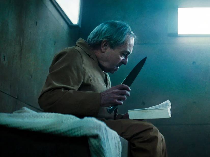An old man with a knife and a book in The Platform