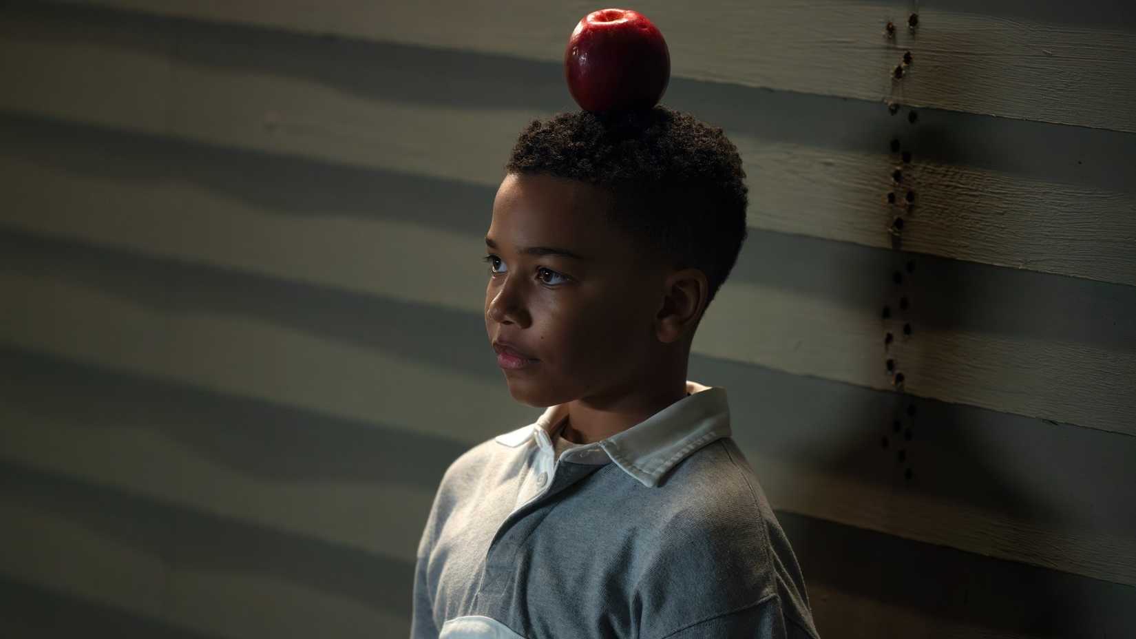 A young John Stewart (Cairo Cash Lee) stands with an apple balanced on his head in Lanterns