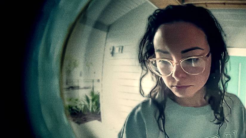 A woman seen through a peephole in Death of a Pastor's Wife