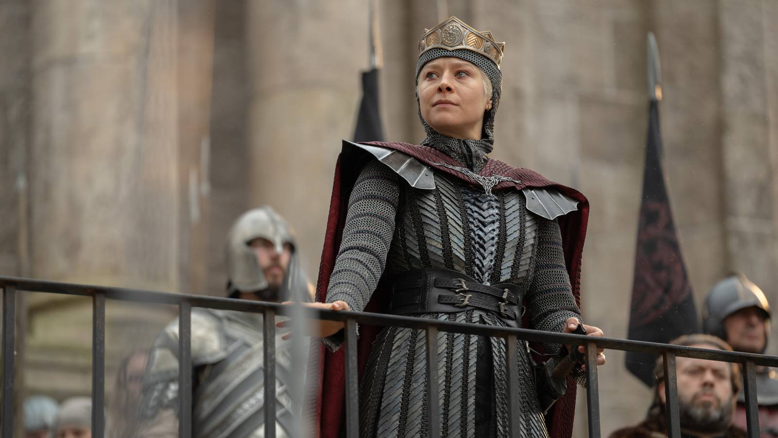 Queen Rhaenyra Targaryen (Emma D'Arcy) looks over a railing while her guards and council stand behind her in House of the Dragon