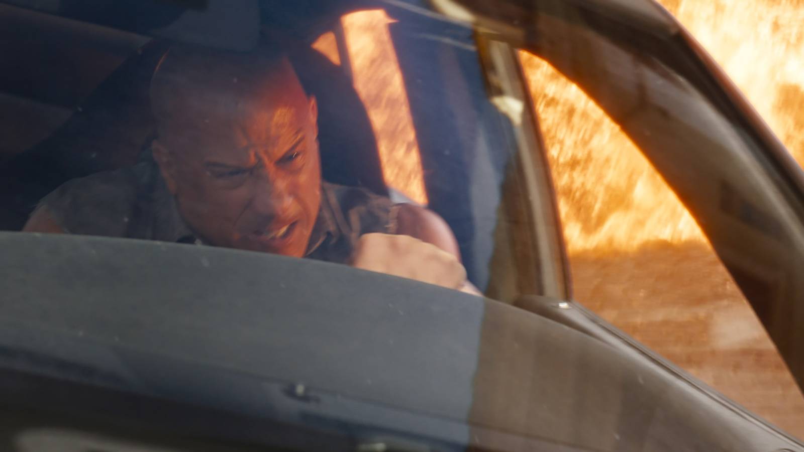 Vin Diesel driving a car and gnashing his teeth as an explosion blows up in Fast X