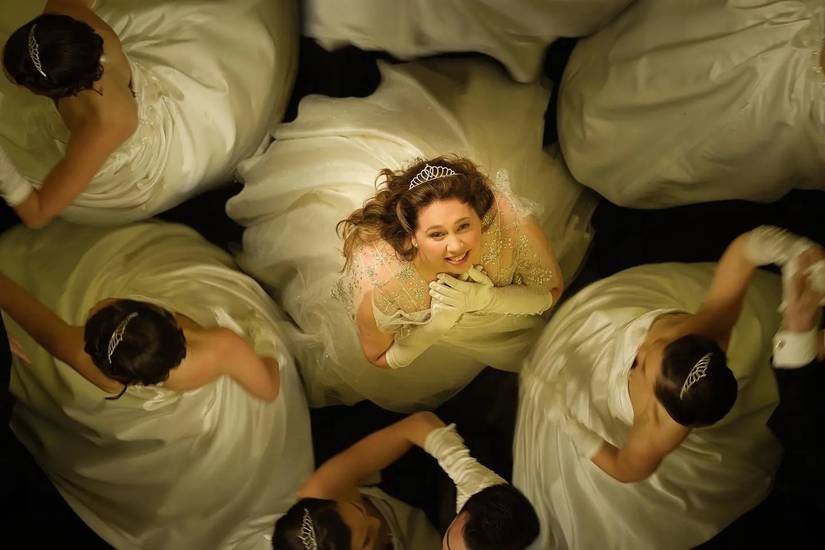A girl wearing a white dress surrounded by other girls in The Deb